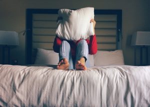 person sitting on bed with pillow on head