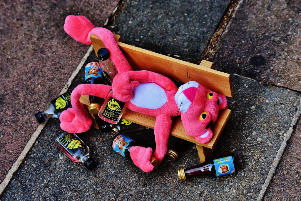 pink panther laying on the bench next to empty bottles